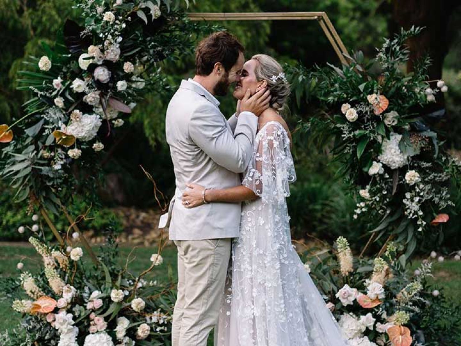 A couple celebrating their wedding, kissing underneath a beautiful flower arrangement. 
