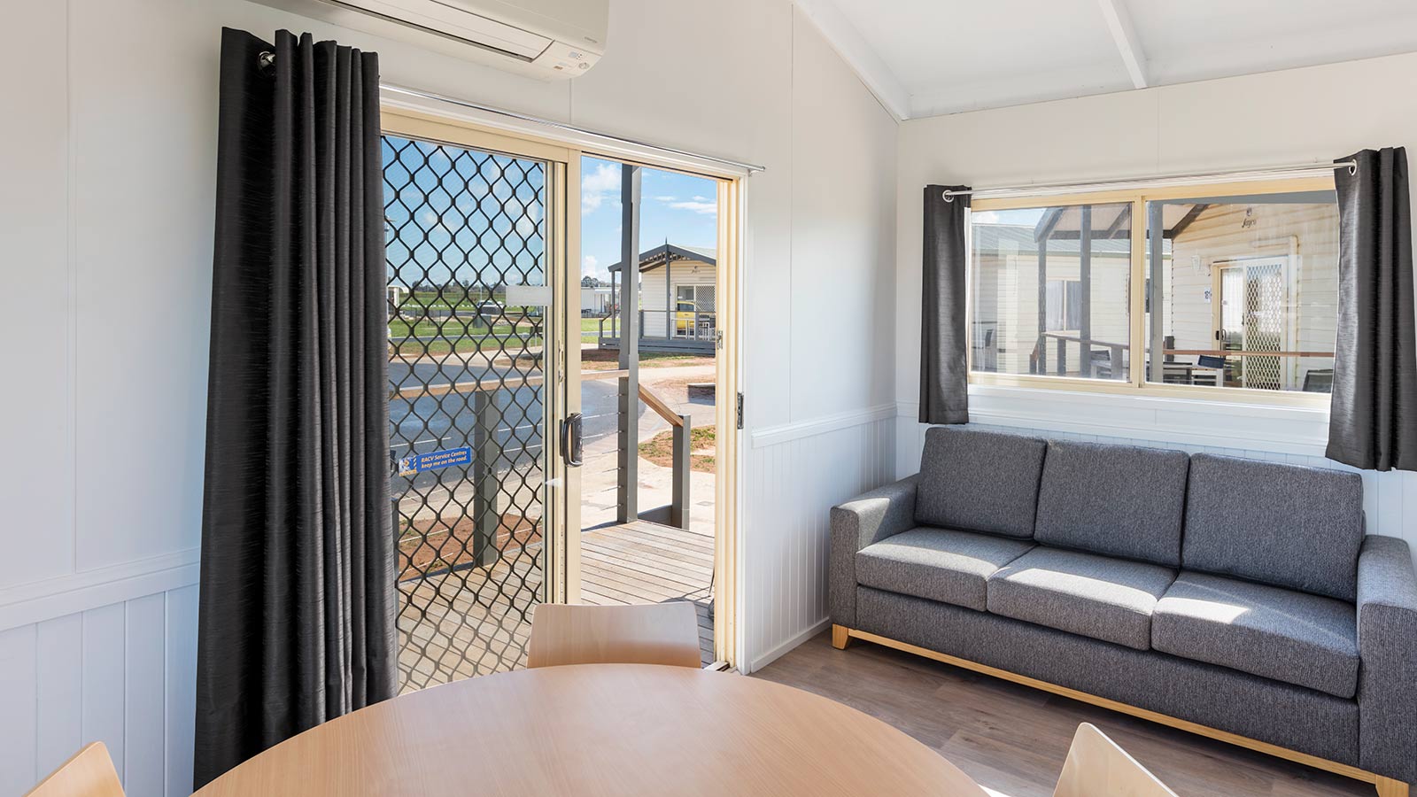 Living area in RACV Cobram Resort's accommodation, featuring a grey three-seat couch and round dining table.
