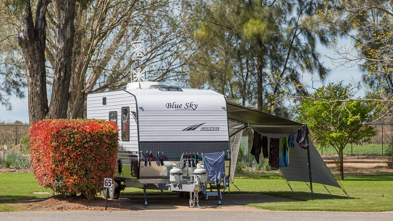 Caravan set up with a washing line next to greenery at RACV Cobram Resort's caravan site.