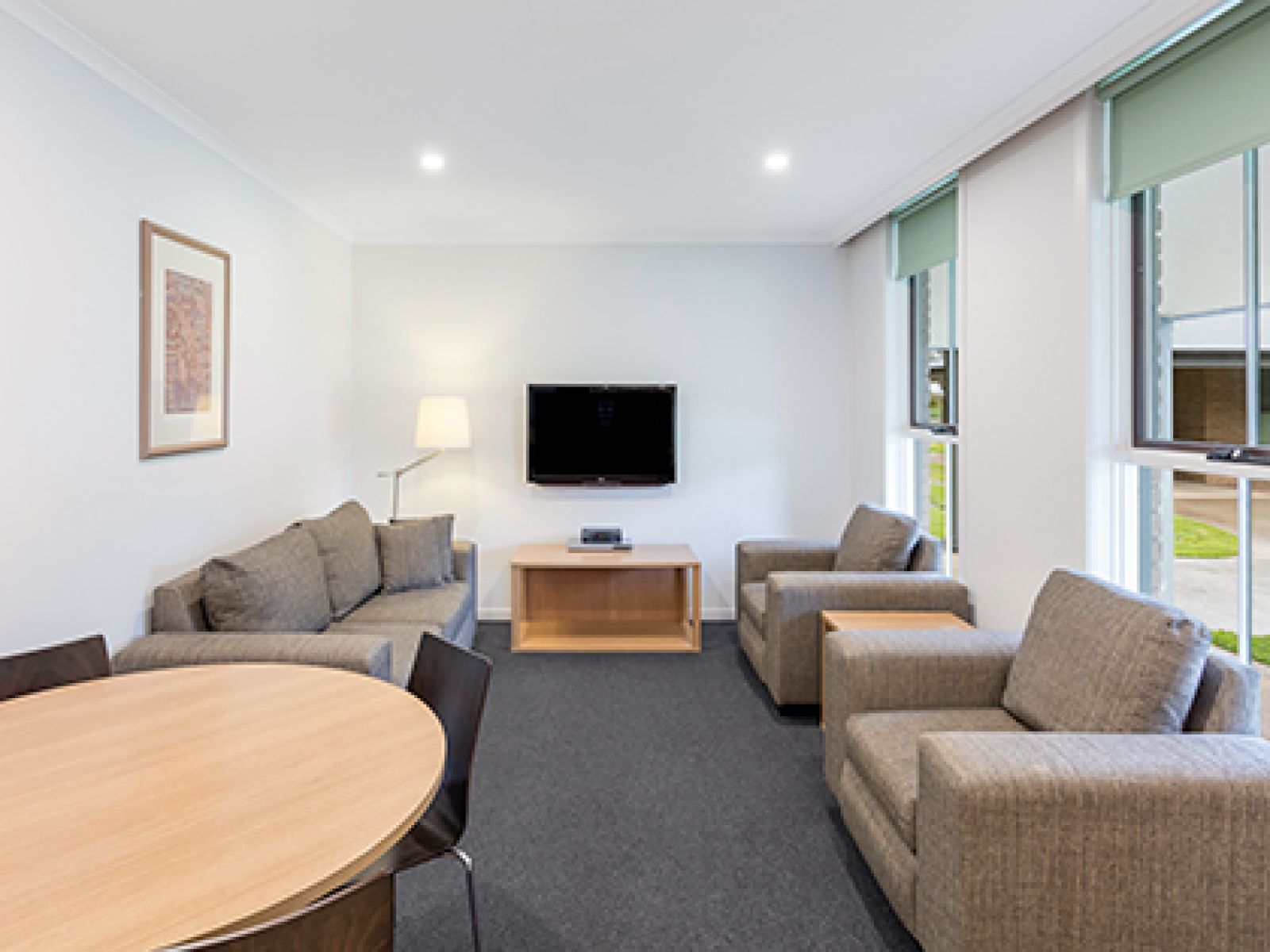 Living area in RACV Cobram Resort's Apartment, featuring grey couches, coffee tables, dining table and television.