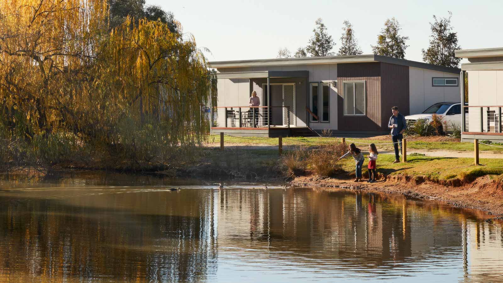 Family with children playing by lake next to cabins at RACV Cobram Resort.