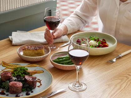 Woman sitting at a table in front of a delicious selection of dishes from the Goldfields dining experiences, holding a glass of red wine.