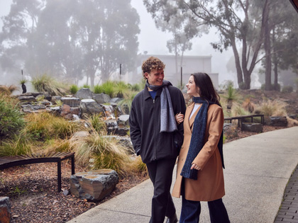 Couple walking together outside in the misty Goldfields grounds rugged up.
