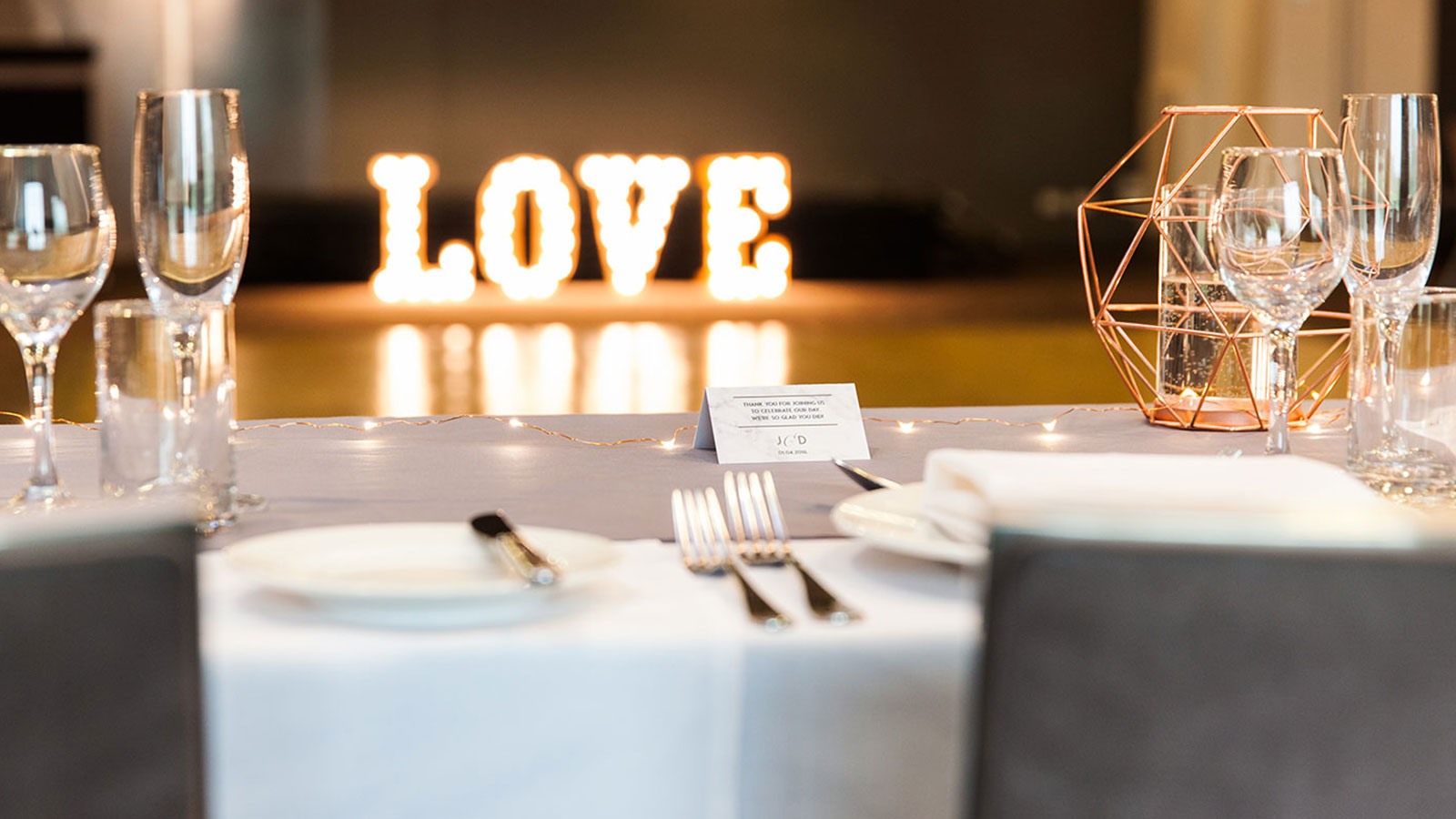 Wedding reception table setup with a lit-up love sign in the back.