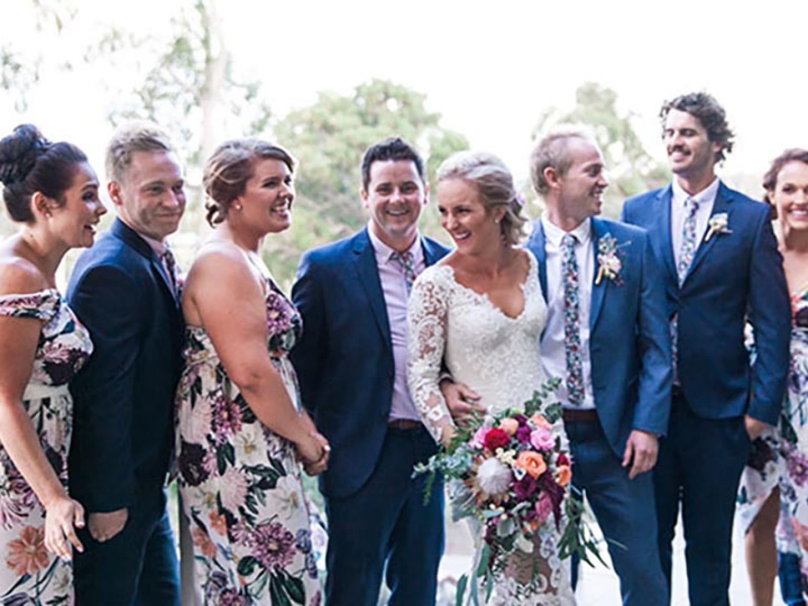 Bridal party celebrating a wedding, with men in navy suits and the women in floral dresses.
