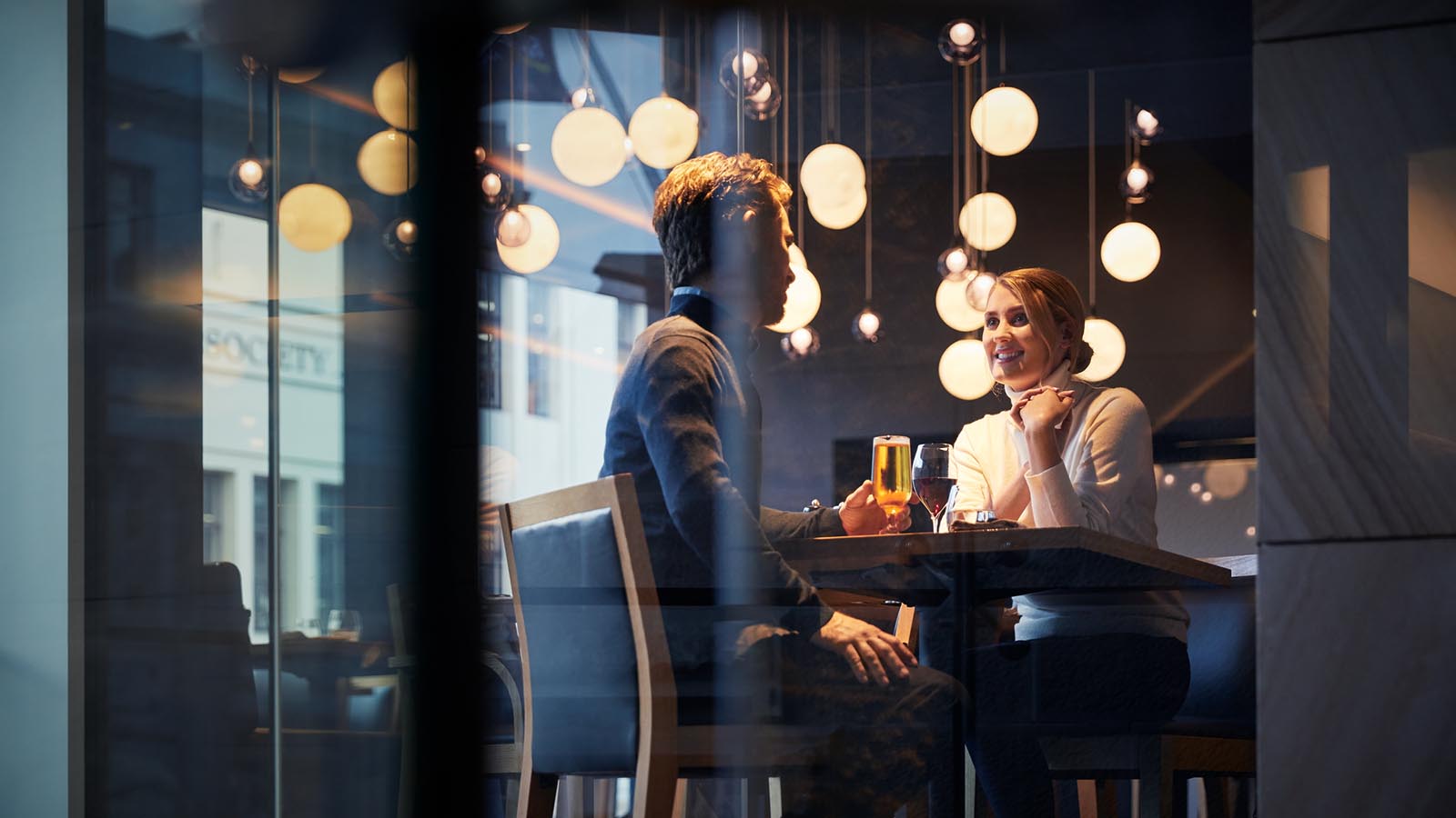 Couple seated at RACV Hobart Apartment Hotel restaurant, shown through window.