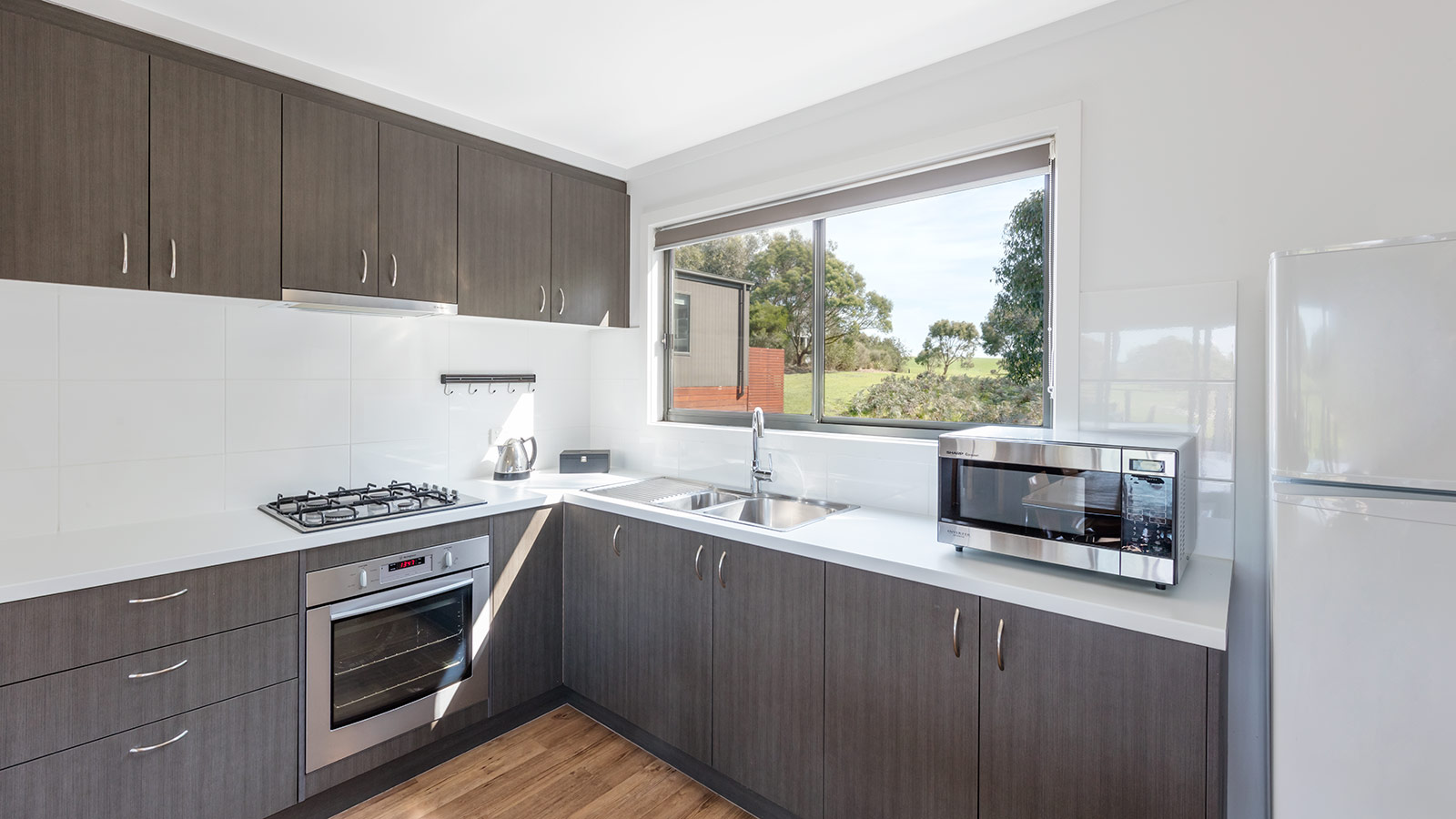 Kitchen in 2-bedroom cabin at RACV Inverloch Resort, featuring a microwave, stove cooktop and oven, sink and kettle.