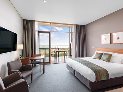 Premium ocean view room at RACV Inverloch Resort, featuring a king bed, couches, television, desk and balcony.