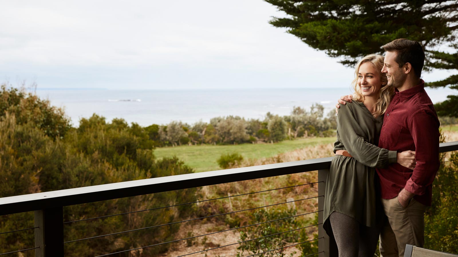 A couple having a cuddle on a balcony overlooking the ocean. 