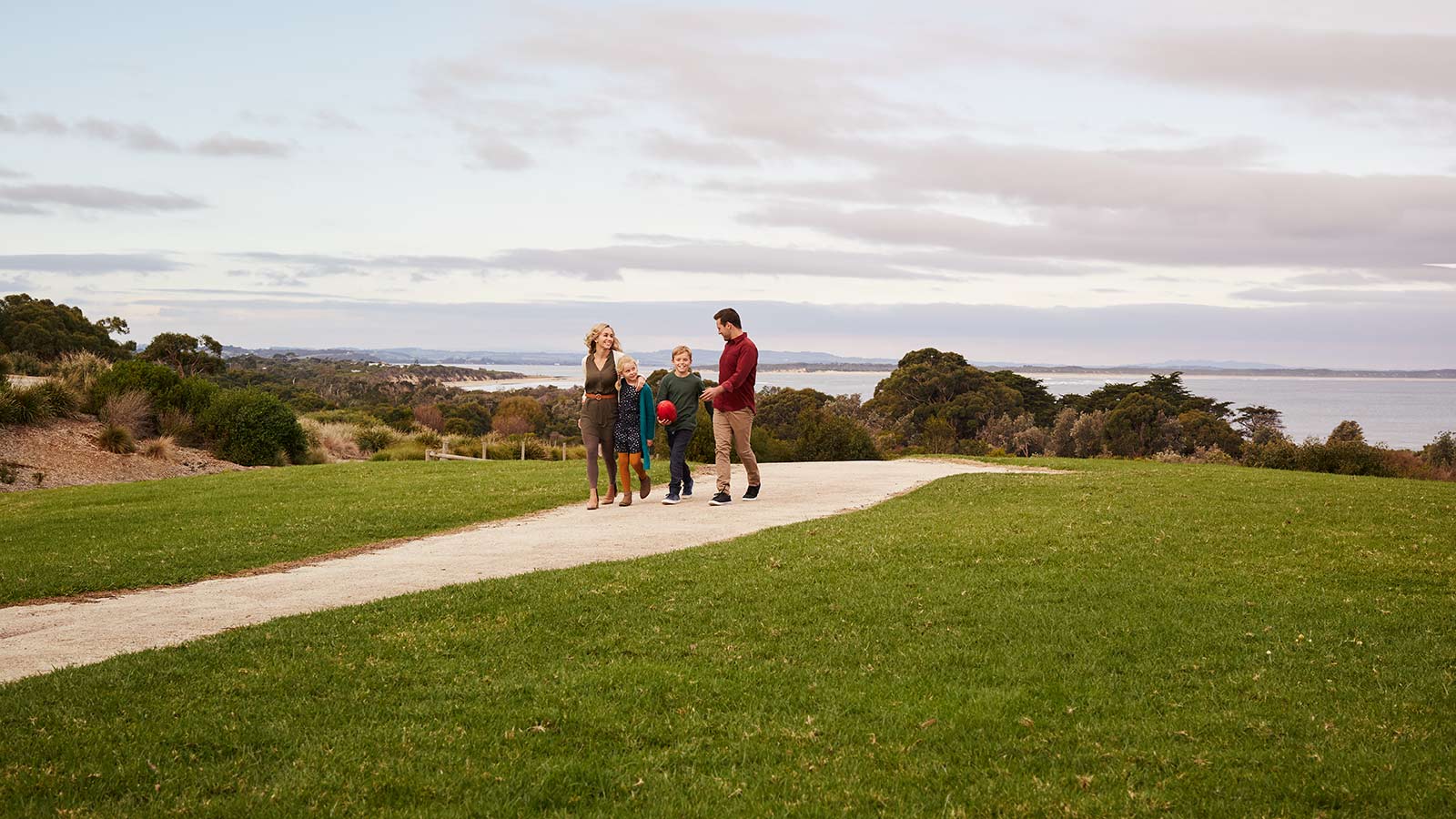 Parents and two kids walking along a path near RACV Inverloch Resort, with the beach behind them.