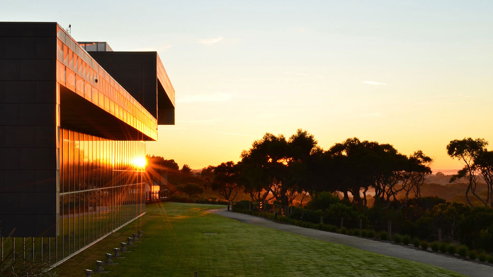 Path surrounded by greenery leading to the main RACV Inverloch Resort building, lit up at night.