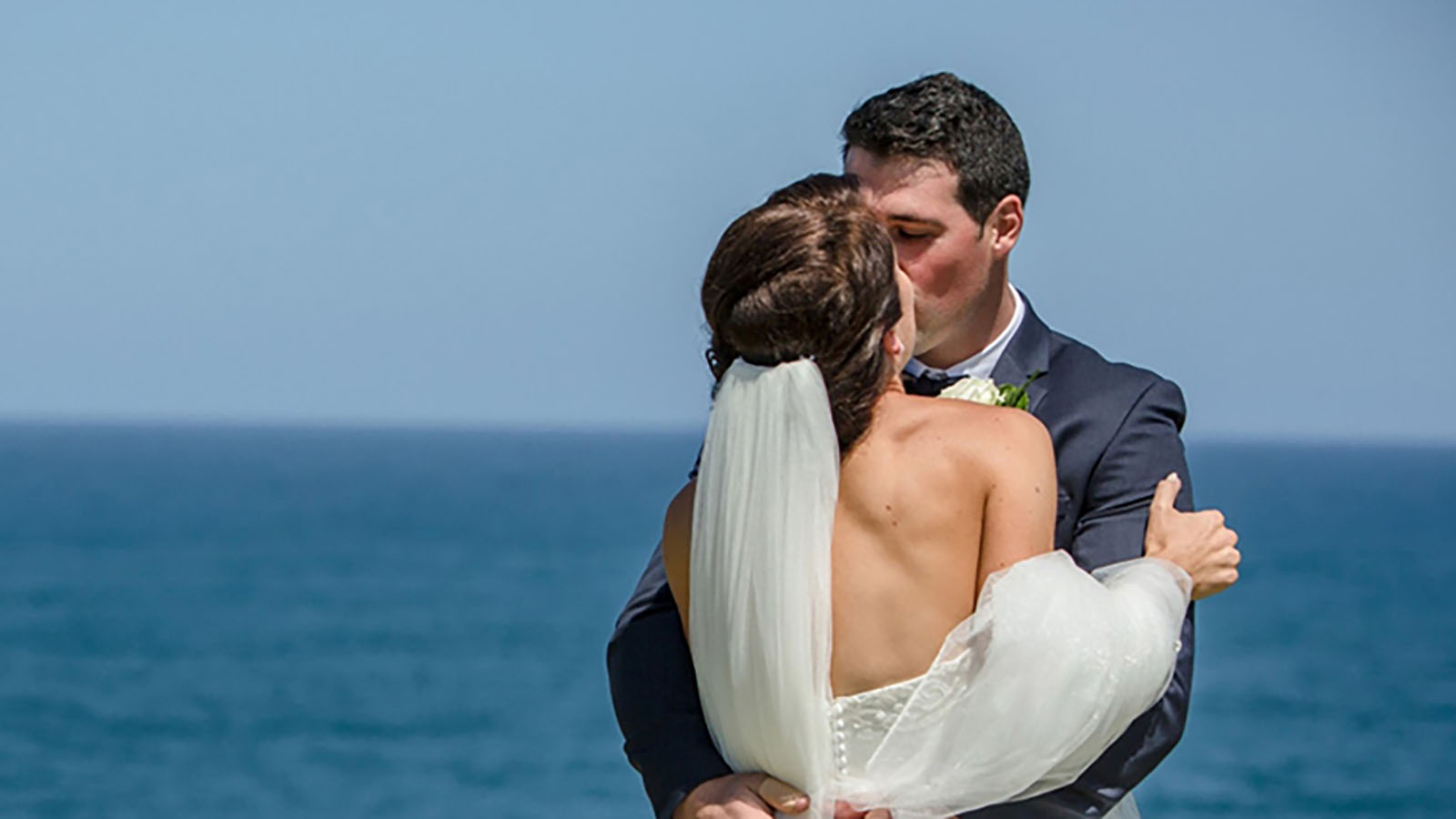 Bride and groom kissing in front of sea near RACV Inverloch resort.