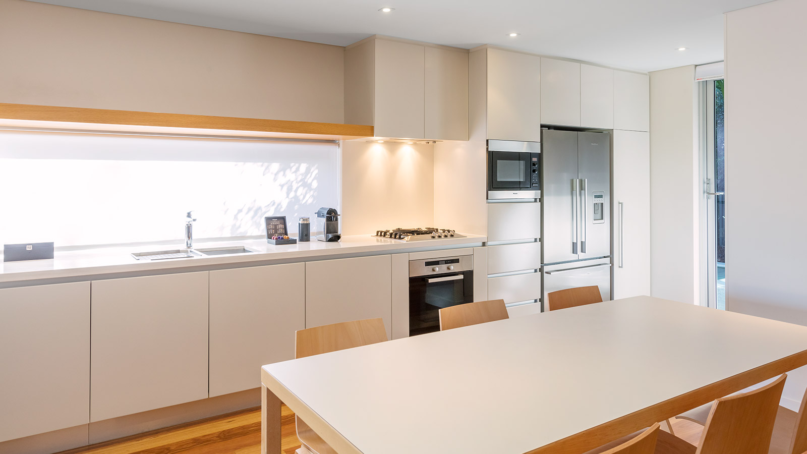 RACV Noosa Resorts Villa kitchen featuring stainless steel fridge, gas cooking stovetop and oven, Nespresso machine and a six-seater dining table. 