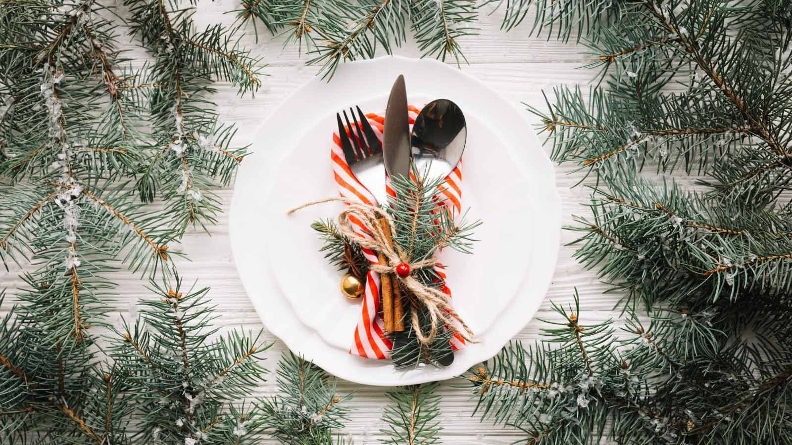 White plate with cutlery, and red and white striped napkin placed on top. Greenery is placed on the table around the plate.