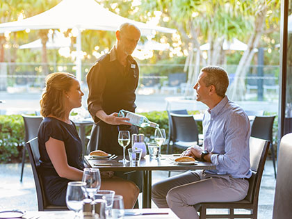 Couple dining by the pool at RACV Noosa Resort while served by a waiter.