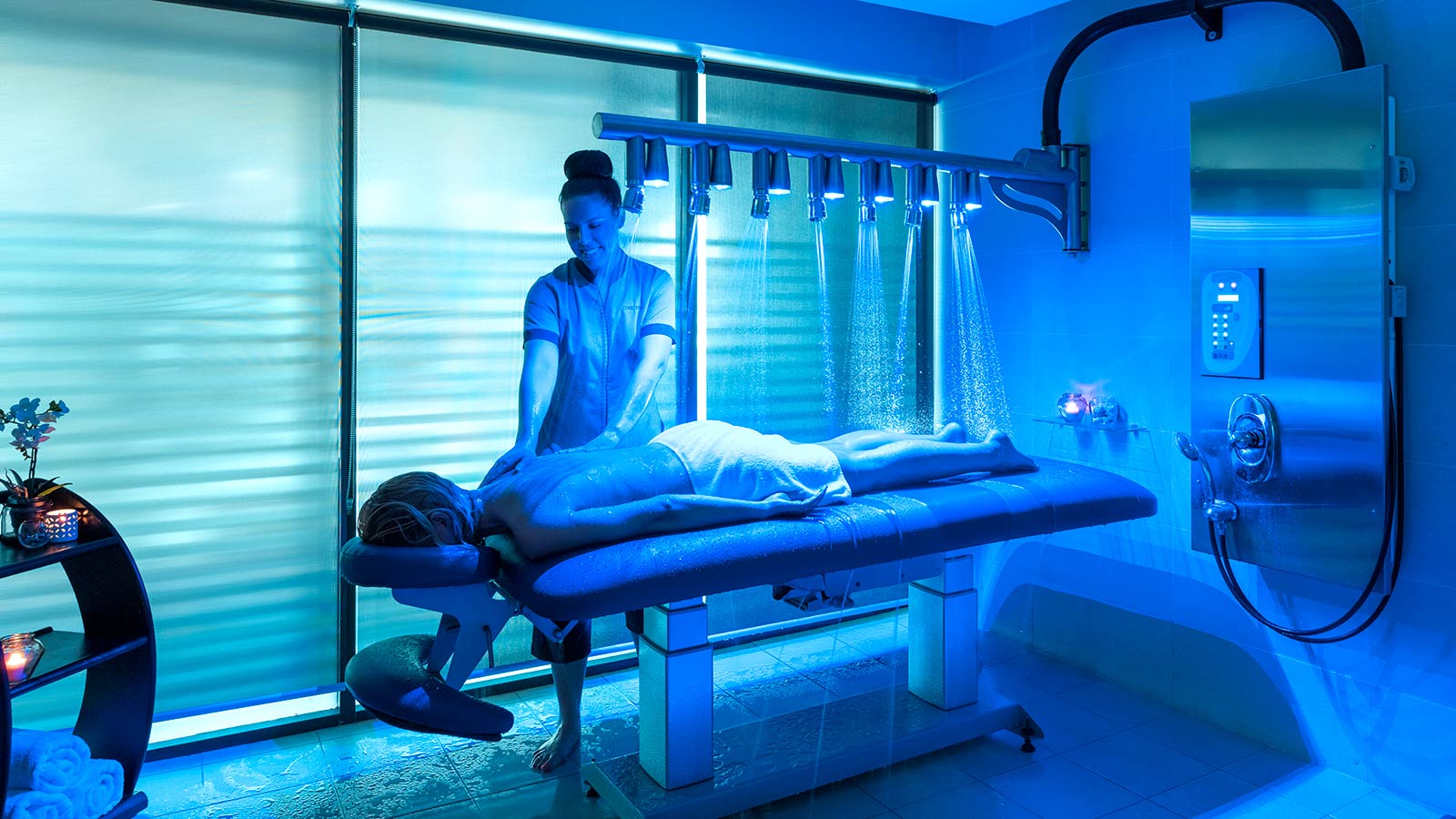 Person laying on their stomach and receiving a back massage at RACV Noosa Resort's One Spa, while showerheads wet their back.