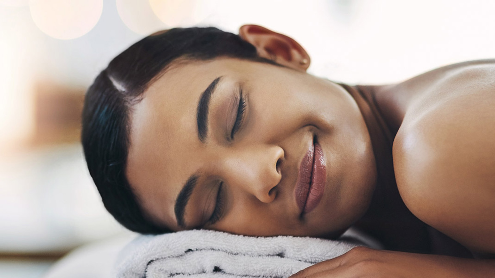 Woman lying down on a massage bed at RACV One Spa, smiling with her eyes closed.