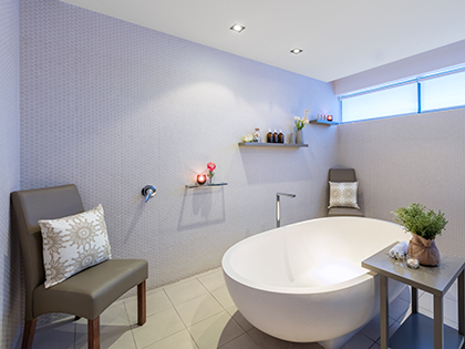 Treatment room at RACV Noosa Resort's One Spa, featuring a bathtub, seats, and shelves with skincare products and lit candles.