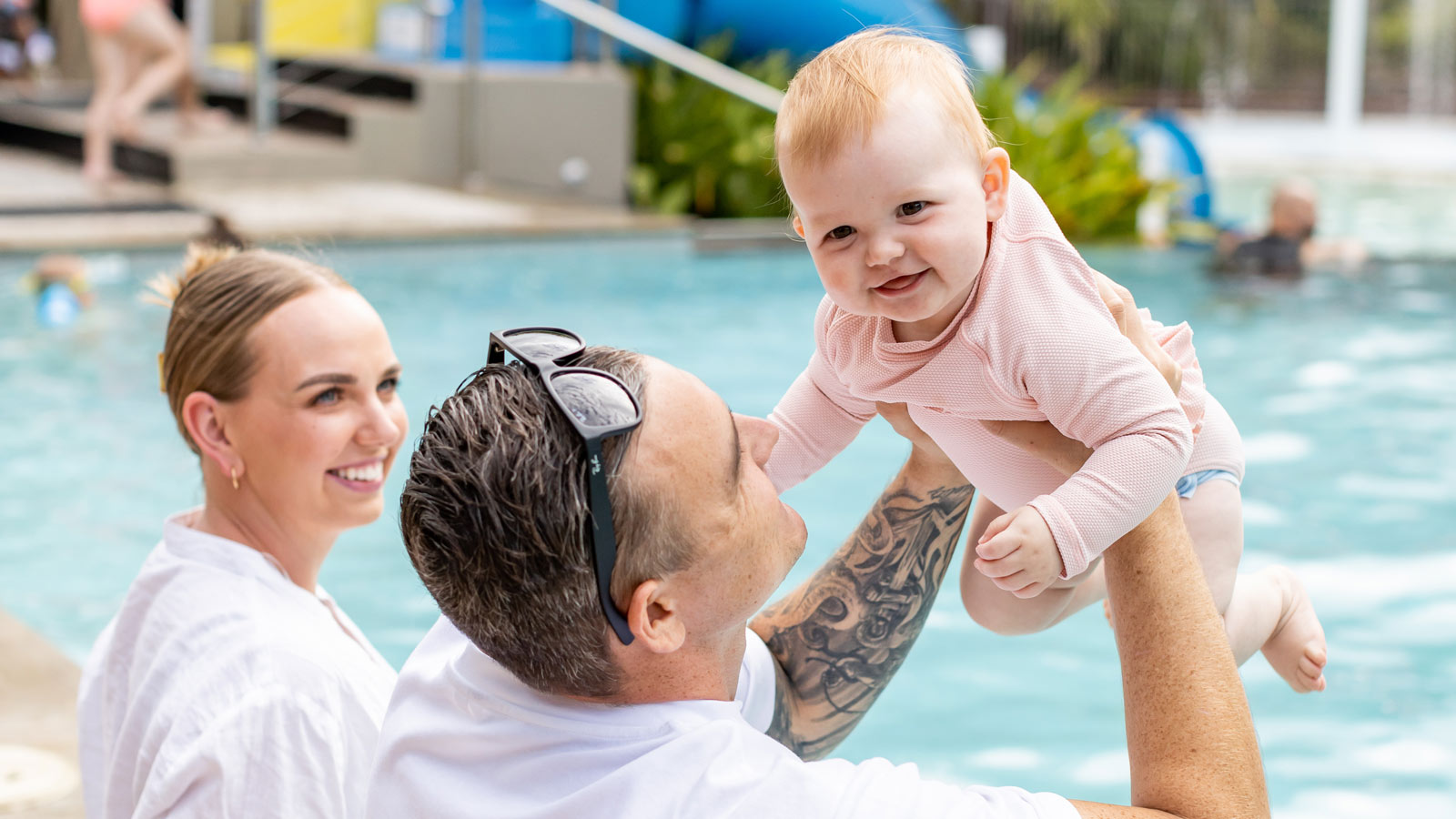 Young couple sitting by the pool with their baby