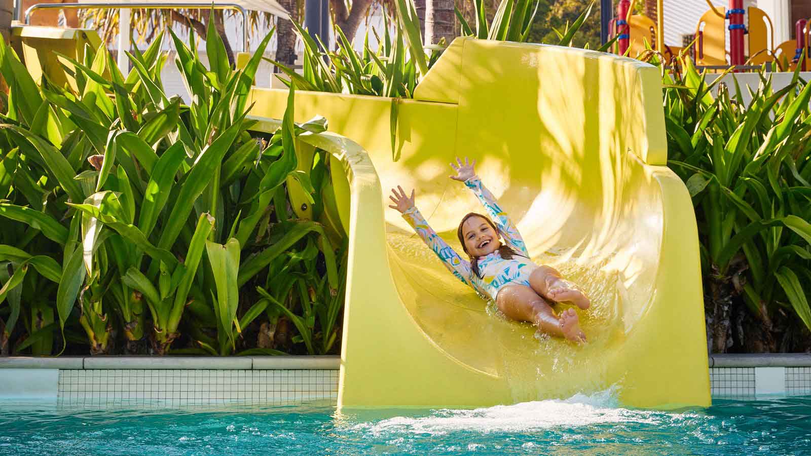 Child with a big smile going down a big yellow pool slide. 
