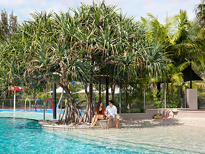 Couple sitting under a tree by outdoor pool at RACV Noosa Resort.