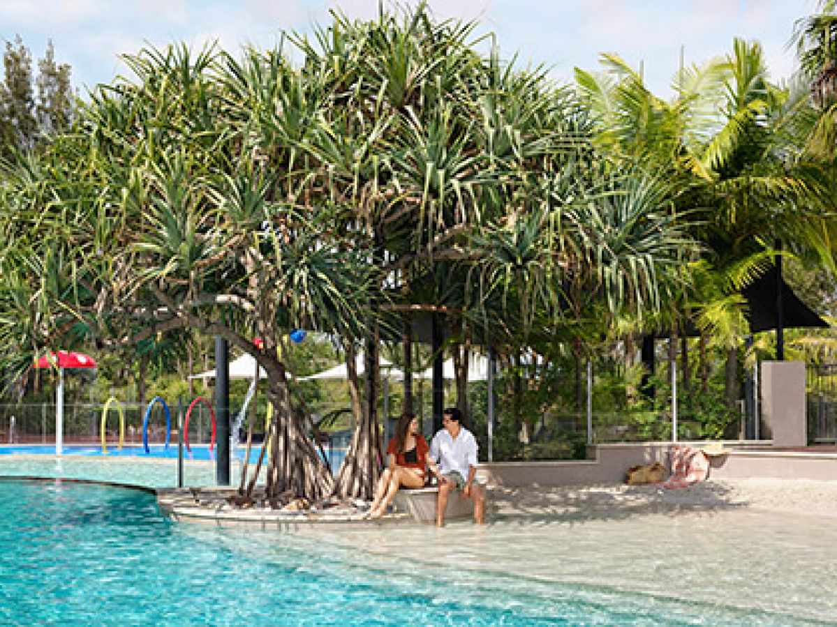 Couple sitting under a tree by outdoor pool at RACV Noosa Resort.
