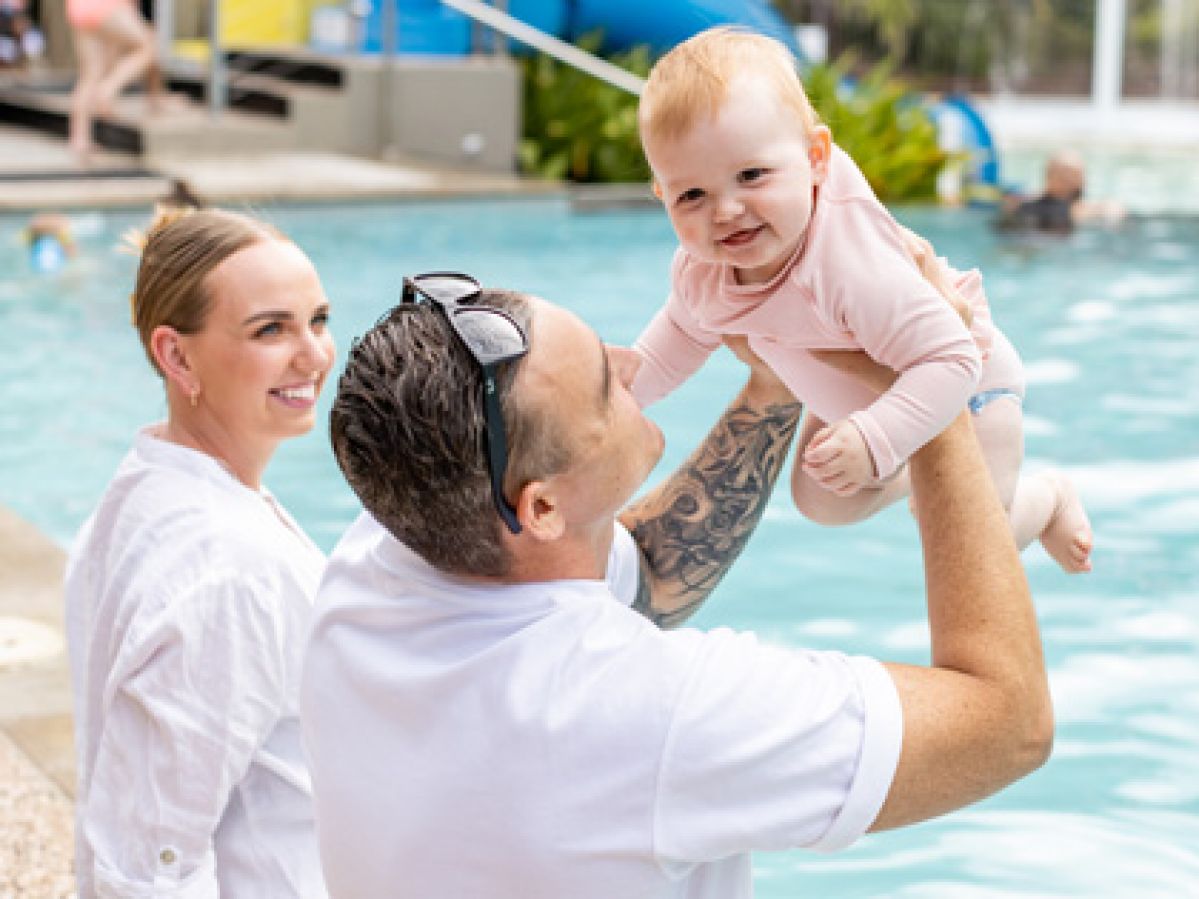 Young couple sitting by the pool with their baby