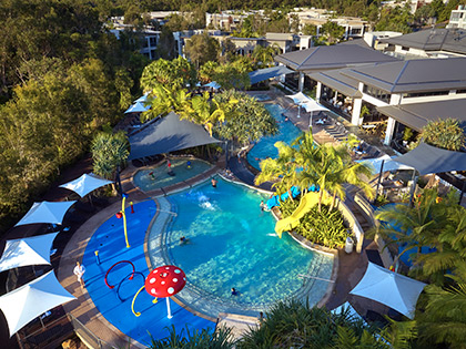 RACV Noosa Resort's pool, surrounded by trees and white umbrellas.