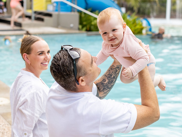 Young couple sitting by the pool with their baby