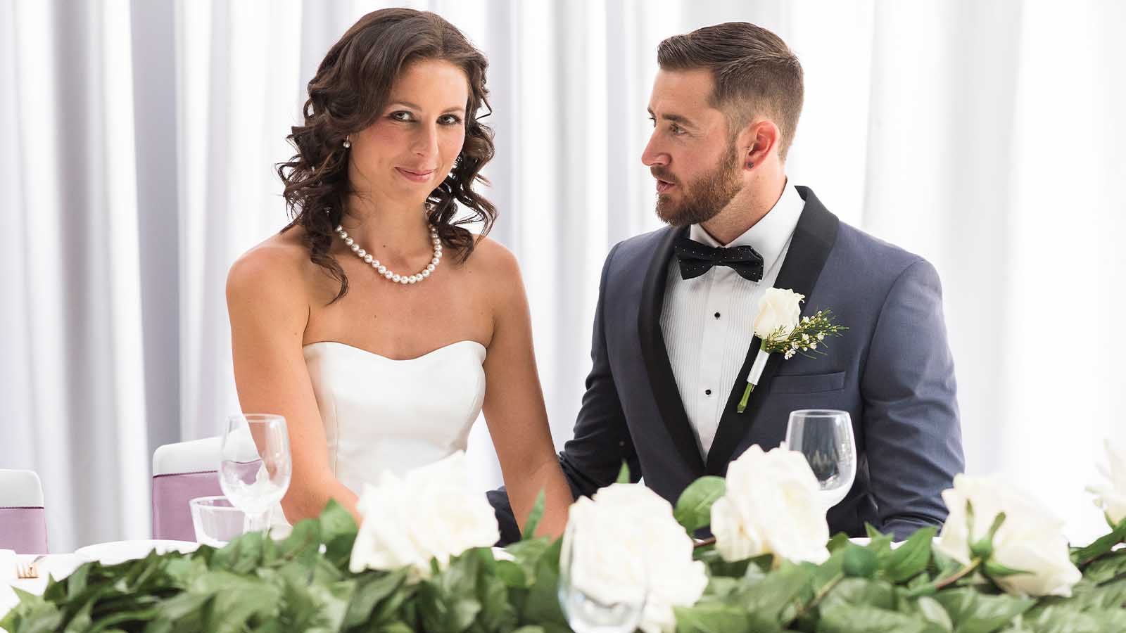 Bride and groom posing while sitting at their bridal table.