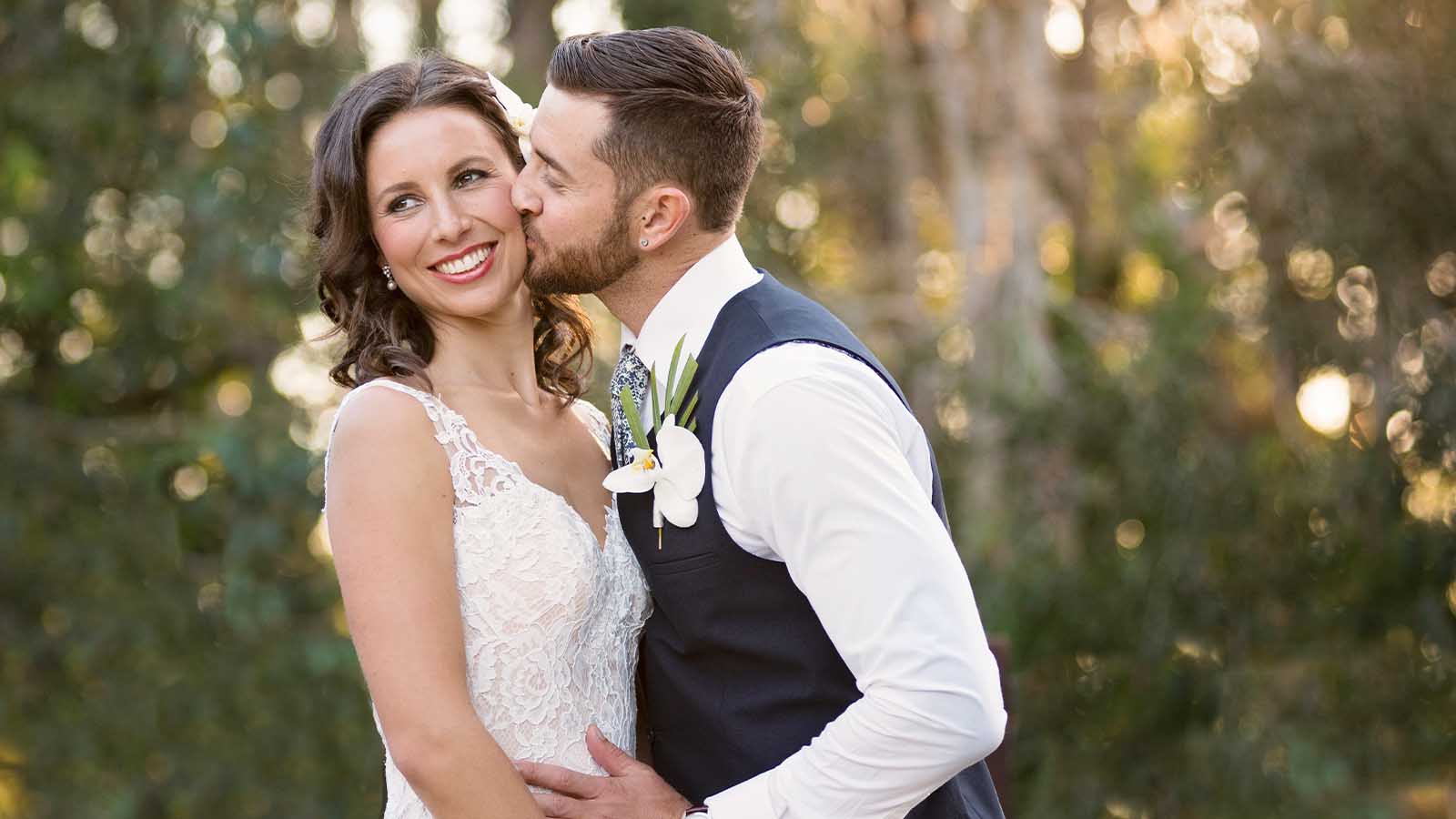 Groom kissing Brides cheek as they pose at the Noosa Resort.