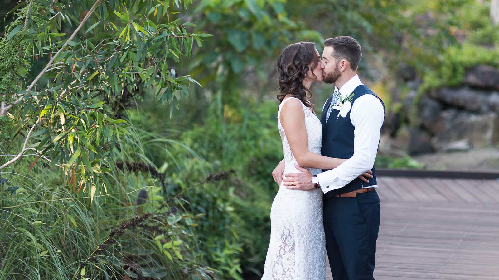 Bride and groom kissing on a deck at the Noosa Resort, surrounded by greenery.