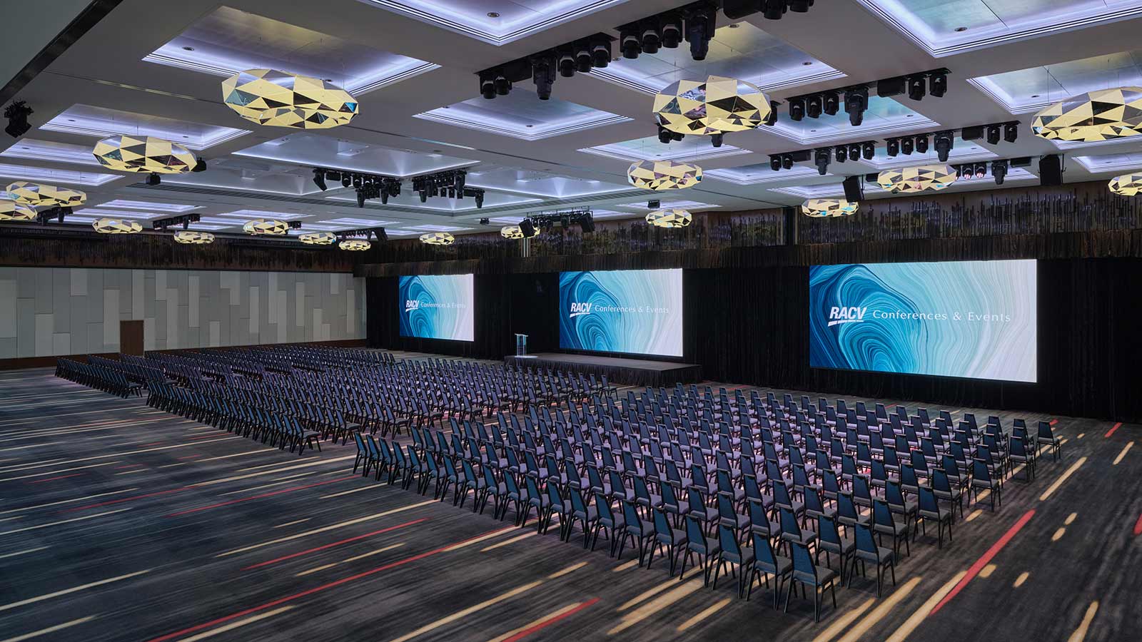Royal Benowa Ballroom at RACV Royal Pines Resort, set up theatre style with three screens behind a stage.