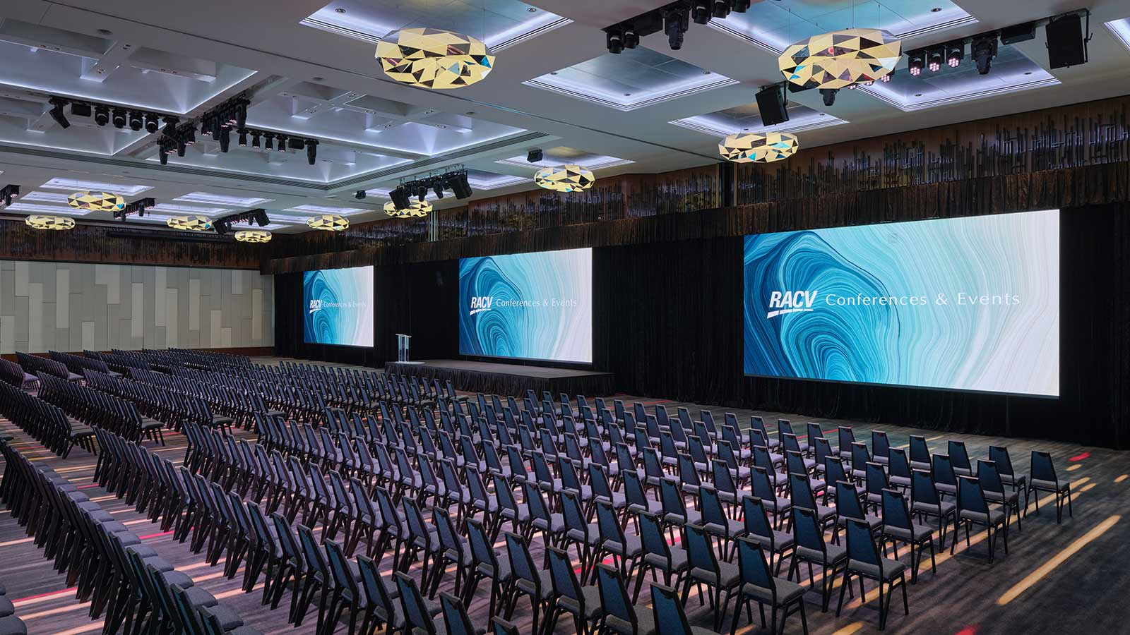 Royal Benowa Ballroom at RACV Royal Pines Resort, set up theatre style with three screens behind a stage.