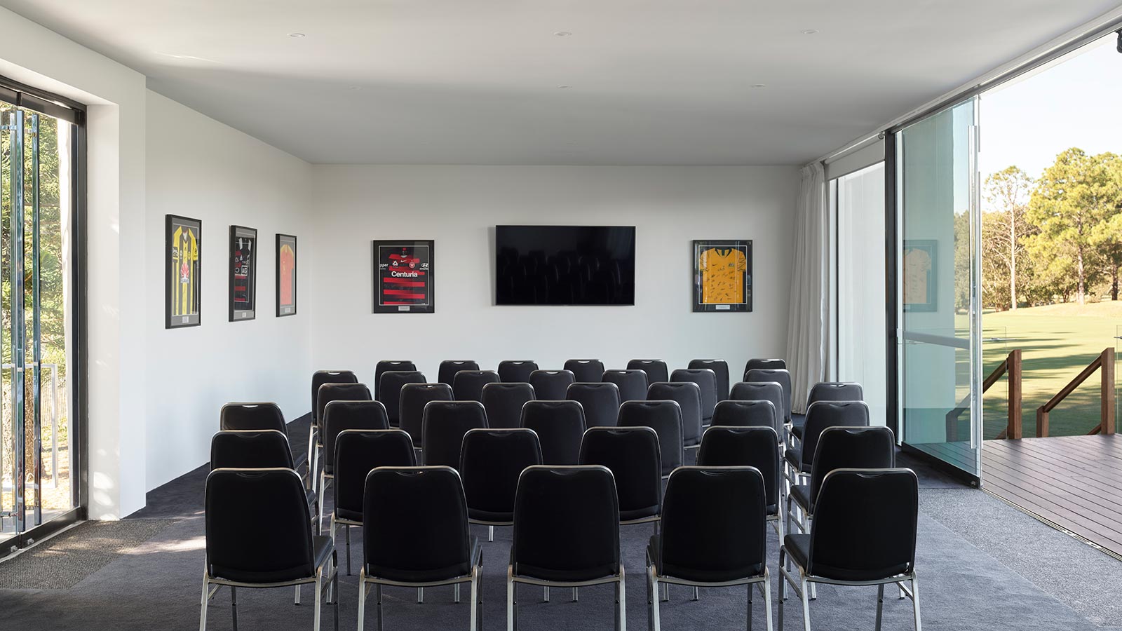 Rows of black chairs facing a television in The Hub at RACV Royal Pines Resort, with framed sports jerseys on the wall.