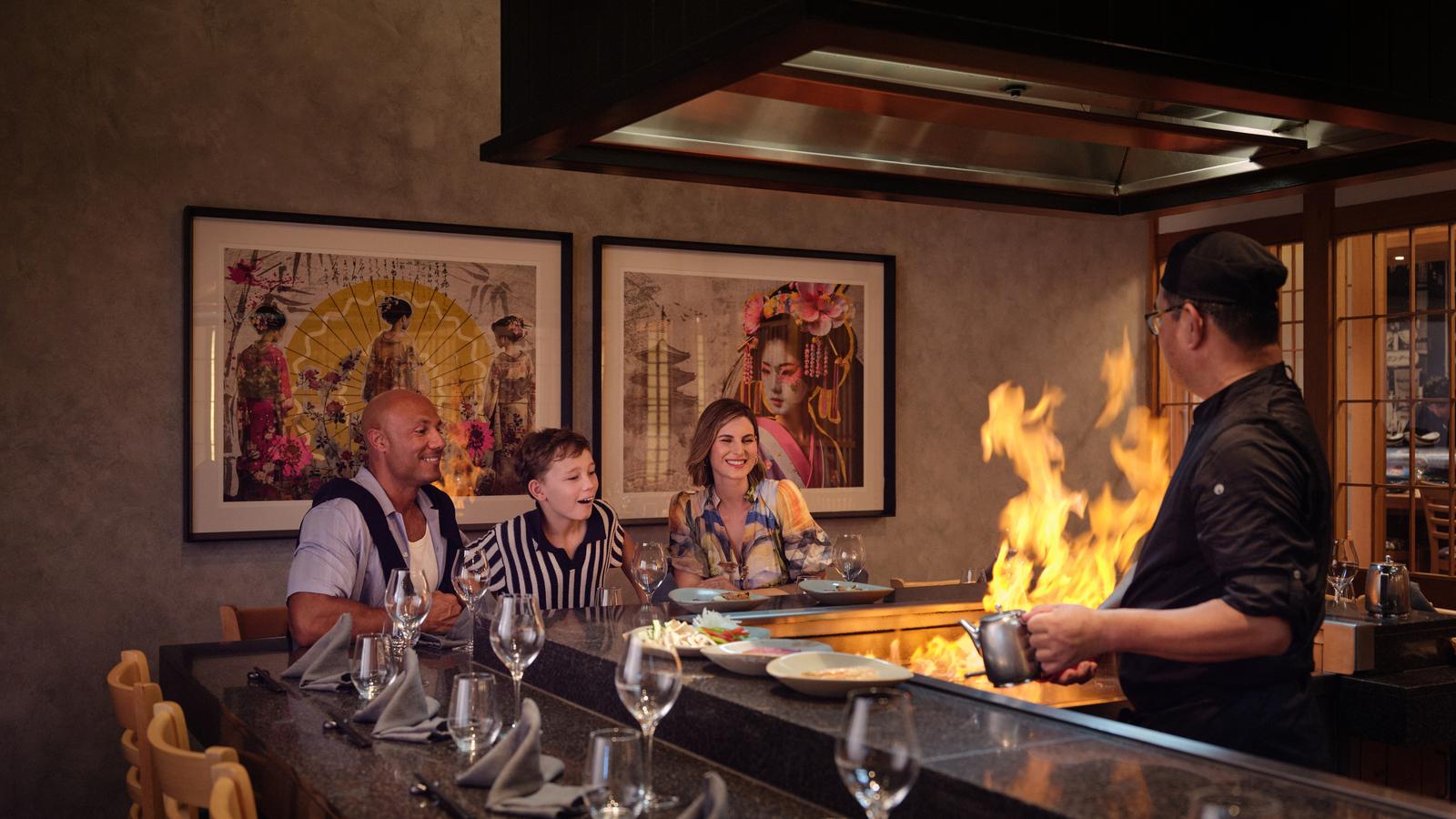 Family enjoying dinner at RACV Royal Pines Arakawa's teppanyaki table while watching chef flambé hot plate.