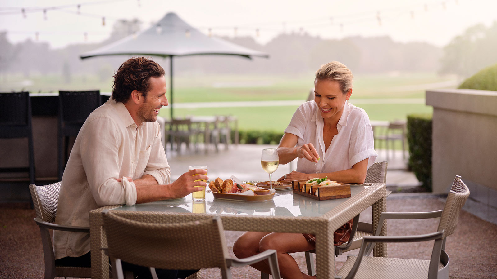Couple laughing and eating sandwiches together in the outdoor area of RACV Royal Pines Resort's Tees' Clubhouse pub.