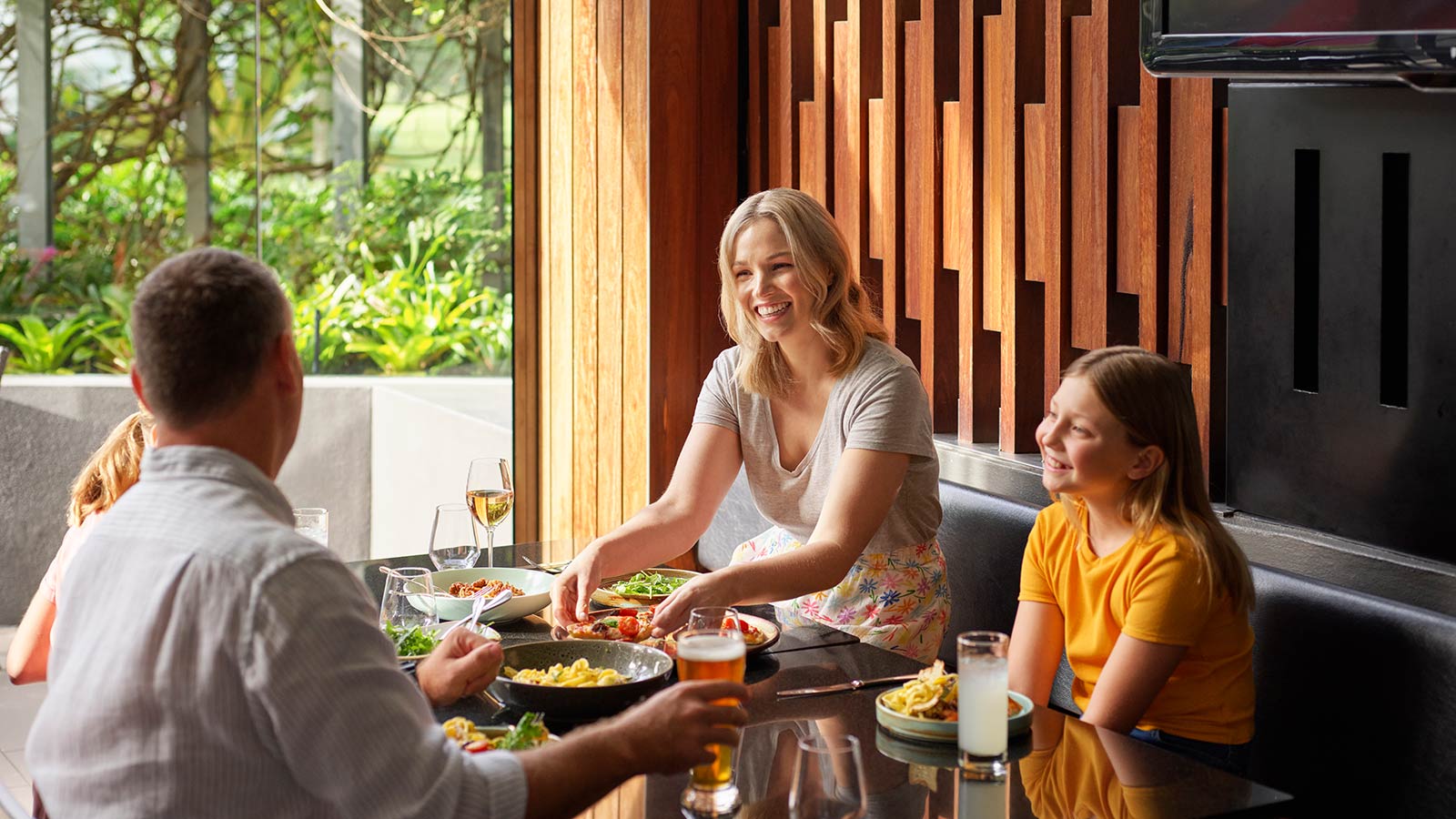 Family eating at RACV Royal Pines resort, next to a window with greenery outside.
