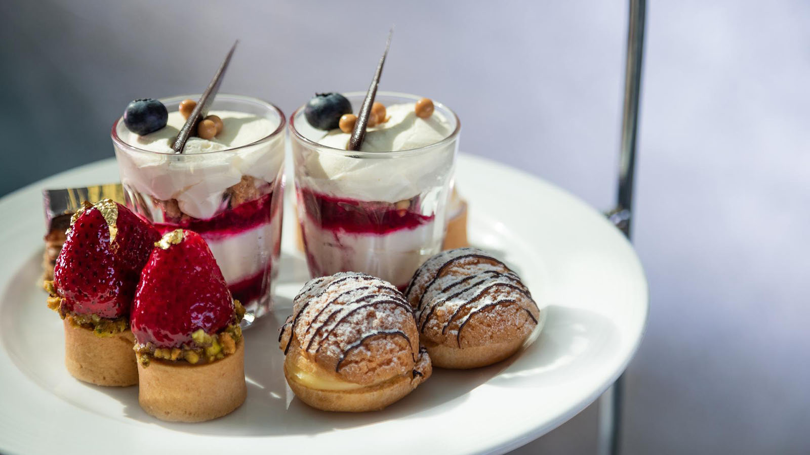 Plated dish of a variety of desserts including cream puffs, strawberry pistachio tarts and fruit yogurt cups.