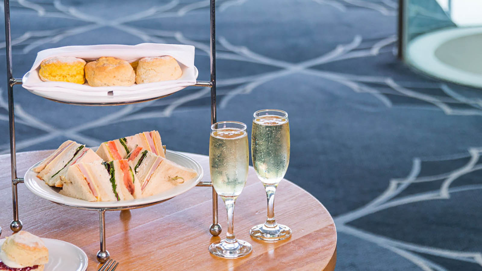 Table featuring two glasses of wine and a tiered tray plated with scones and finger sandwiches.