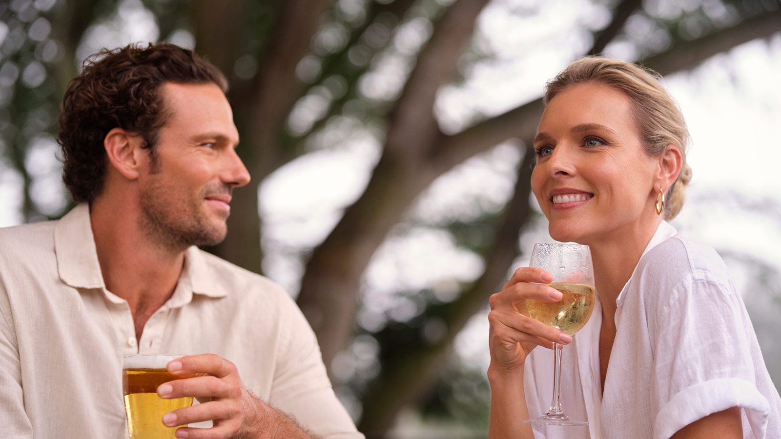 Couple smiling and holding glasses in the outdoor area of RACV Royal Pines Resort's Tees' Clubhouse pub.