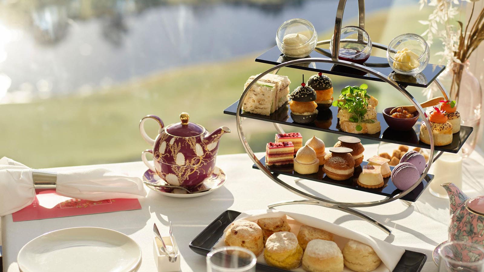 Table featuring RACV Royal Pines Videre high tea setup with teapots, scones, and a tiered tray of desserts, savoury bites, jam, cream and butter.