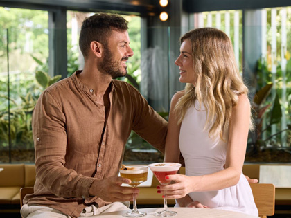 A couple smiling at eachother enjoying a cocktail.