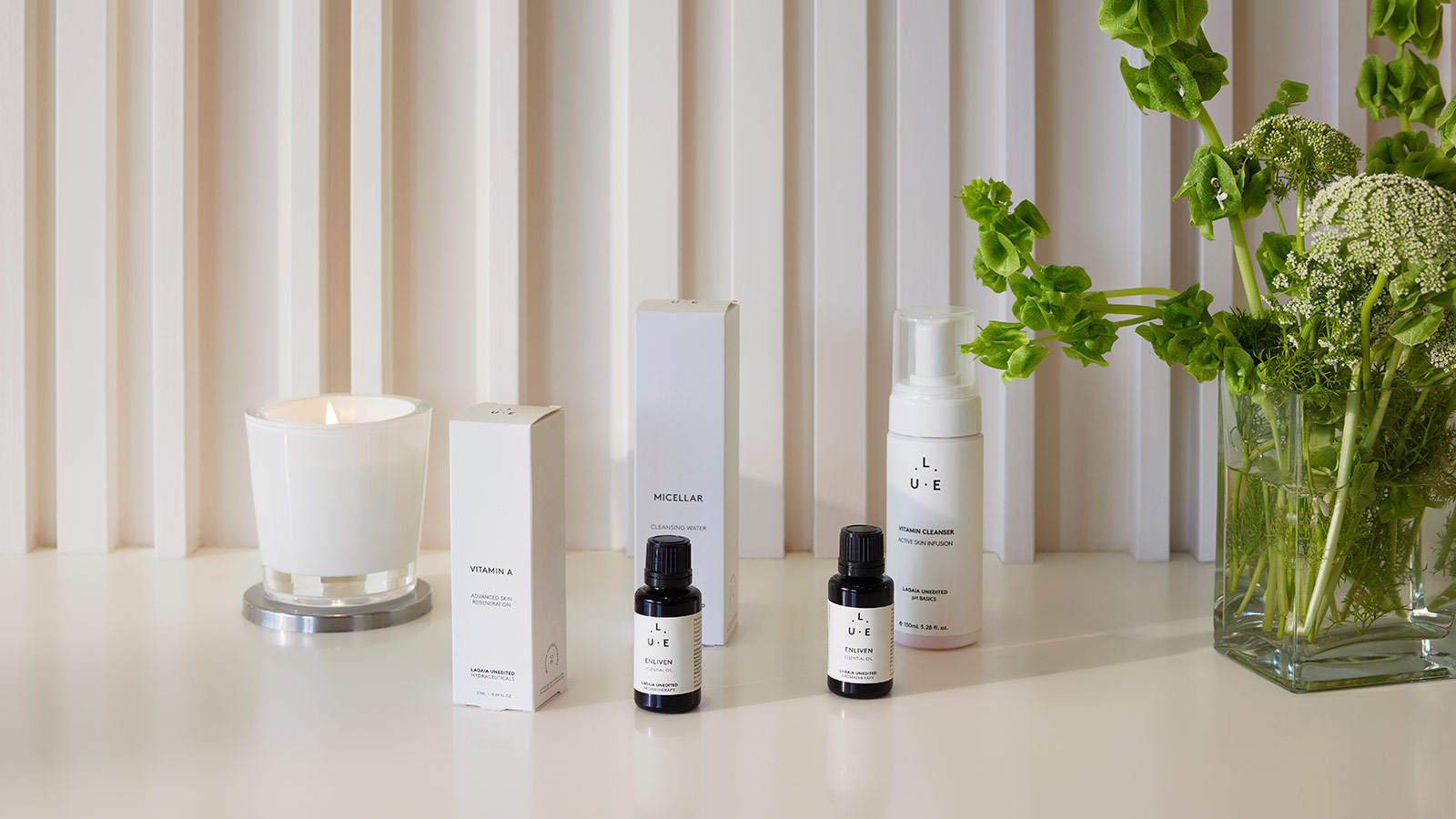 Skincare products and essential oils on a bench at RACV Royal Pines Resort's One Spa, next to a lit candle and a bouquet of flowers.