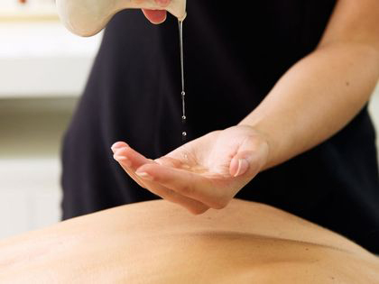 A person pouring oil into their hand in preperation to give a massgae.