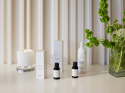 Skincare products and essential oils on a bench at RACV Royal Pines Resort's One Spa, next to a lit candle and a bouquet of flowers.