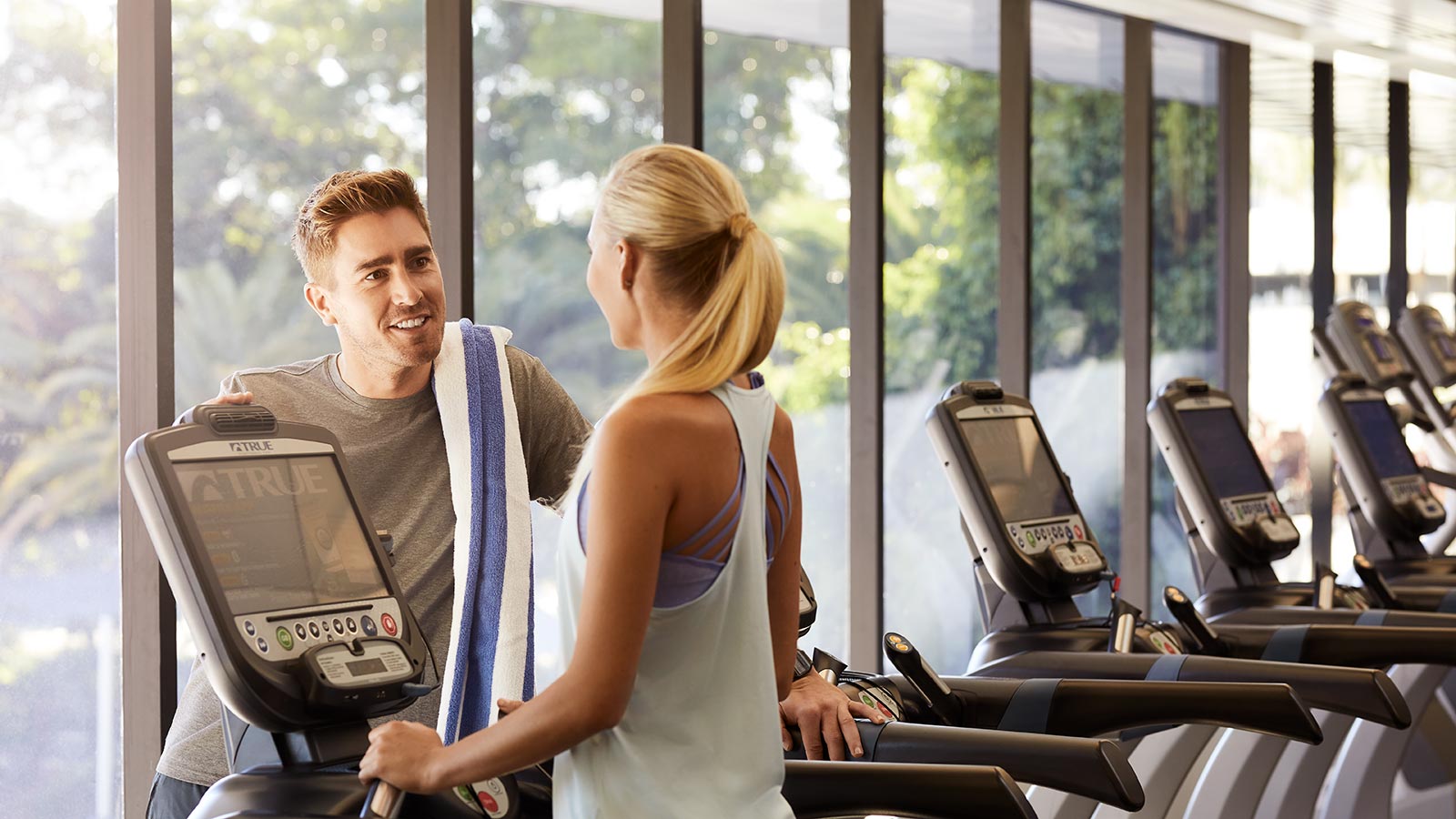 Two people smiling together by the treadmills at RACV Royal Pines' One Lifestyle fitness centre.