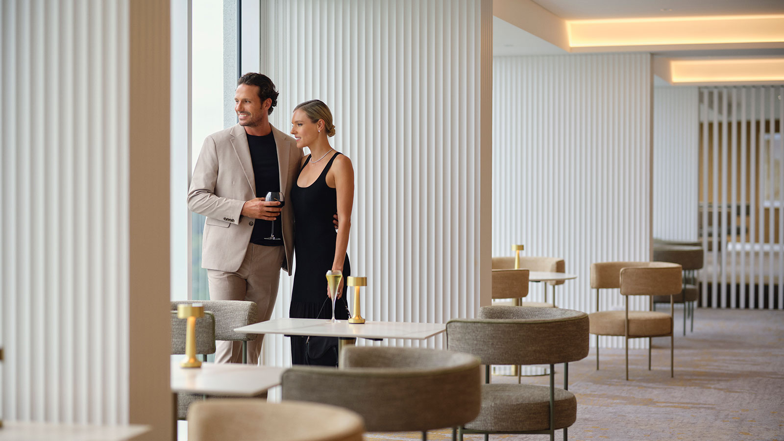 Couple looking out a window from the Executive Lounge at RACV Royal Pines Resort, with drinks in their hands.