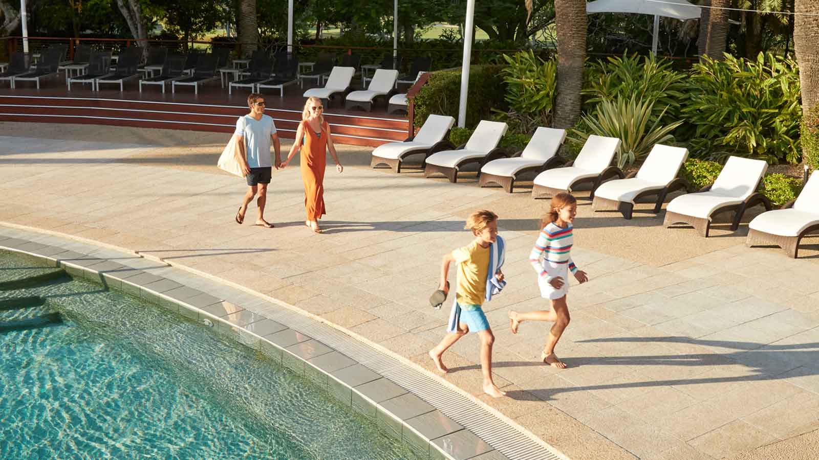 A family walking poolside at RACV Royal pines on a sunny day. 