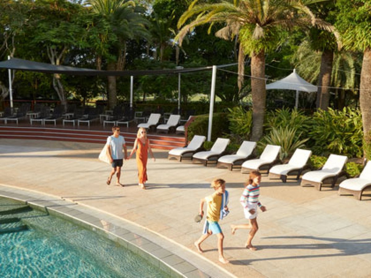 Family walking by a resort pool on a sunny day.